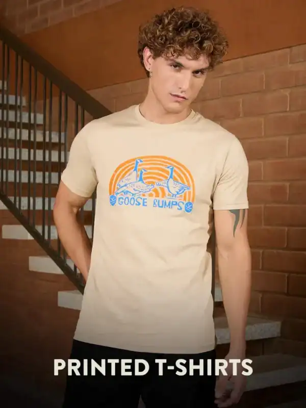 Beige printed T-shirt with an orange-blue “Goose Bumps” graphic on the chest, worn by a man with curly hair.